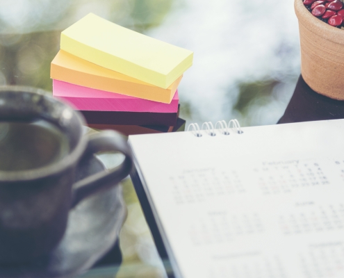 Image of calendar on table with cup of coffee, post it notes, and a cactus plant.